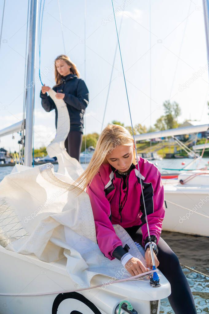 Before the competition on sailing boats two cute girls athletes equip their sailing yacht