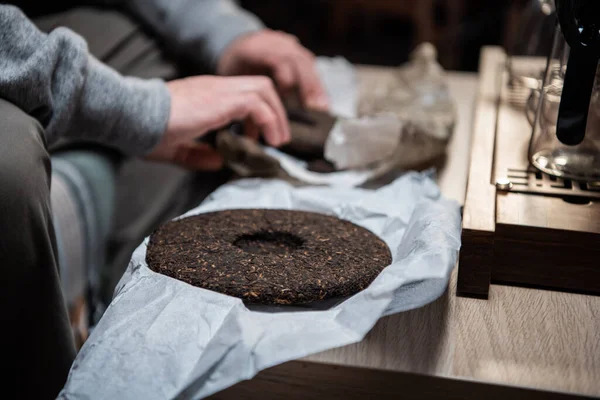 Ein Stück roher Pu-Erh-Teekuchen in den Händen eines Teemasters vor einer echten chinesischen Teezeremonie in einem Teehaus. — Stockfoto