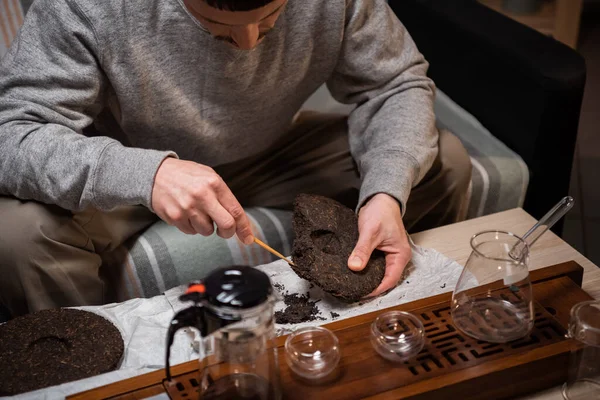 Ein Mann bereitet rohen reifen Tee für eine Teezeremonie zu. Sucht sich ein Stück Tee mit einer Teenadel aus. Hände aus nächster Nähe. — Stockfoto