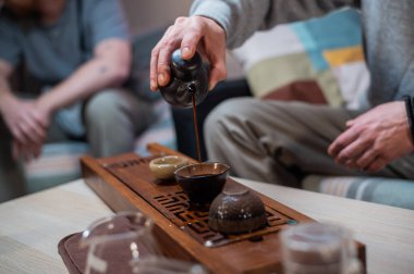 Erkek elleri cam bir kaseye mis kokulu kehribar çayı döker. Çay seremonisi ve geleneksel Çin usulü tatma..