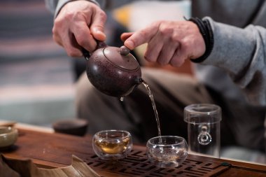 Çay dükkanında çay seremonisi ustasının elleriyle yakın plan çekimde, bambu tablasında özel fincanlar tatmak için çay doldururken..
