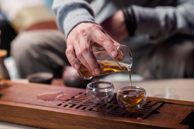 Bir adam sıcak bir içeceği fincana doldurmak için bir bardak çay tutar. Çin 'de gerçek bir çay seremonisinin sırları..