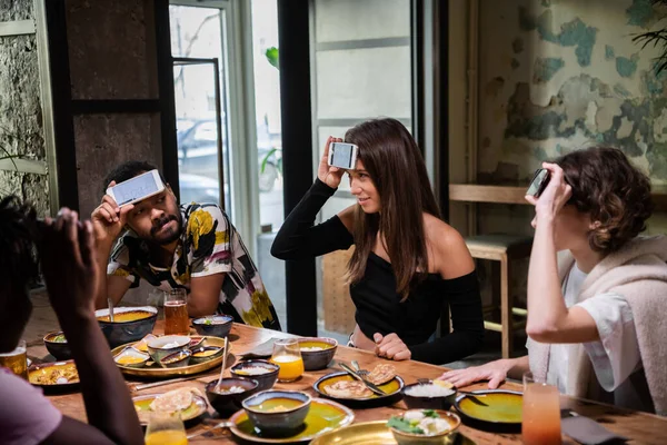 Des jeunes amis multiculturels assis à table dans un café et secouant la tête, tout en jouant à un jeu de devinettes — Photo