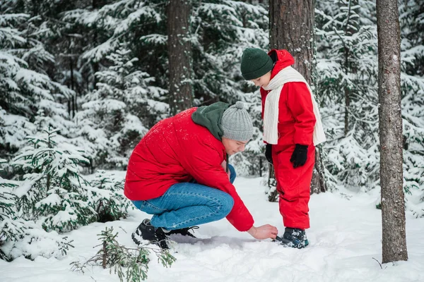 Заботливый отец настраивает своих сыновей зимний костюм во время прогулки в парке зимой — стоковое фото