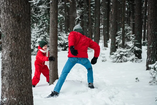 Зимой в лесу мужчина в пиджаке играет на свежем воздухе со своим сыном в комбинезоне, чтобы согреться. — стоковое фото