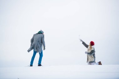 Karlı bir ovanın beyaz arka planında, bir çift sevgili bir randevu sırasında koşar ve sarılır.
