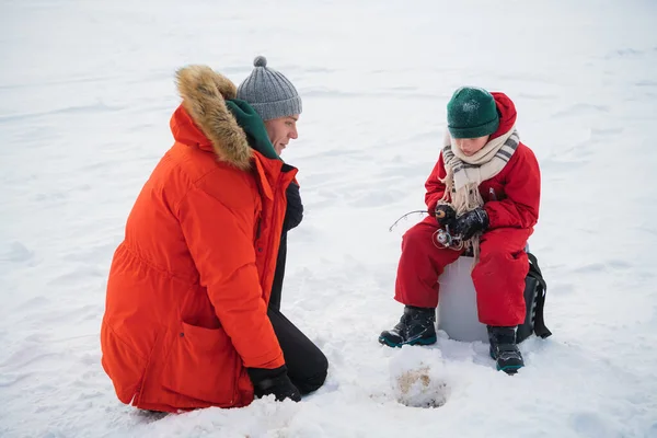 A young father teaches his son the basics of winter fishing on the ice of a lake in the village
