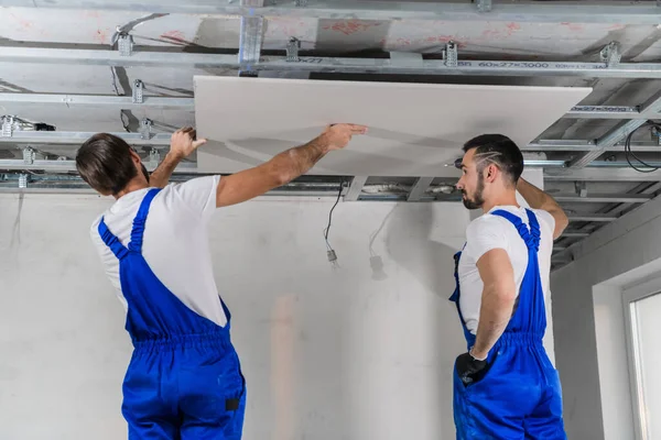 Artesanos en overoles azules haciendo techo en habitación de apartamentos — Foto de Stock