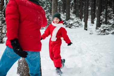 Kışın, genç bir baba ağaçların arasındaki ormanda oğluyla kovalamaca oynar.
