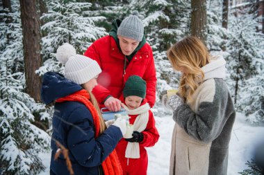 Çocuklu genç bir aile için kış masalı, bir oğlan ve bir kız, izin gününde ormanda yürüyorlar. Kar yağışı ve termosta sıcak çay.