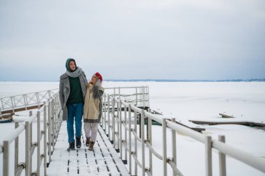 Aşıklar birbirlerini sevgiyle ısıtır ve göl kıyısındaki bir kış yürüyüşünde sarılırlar.