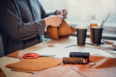 Ön planda iplik bobinlerinin derinliği olan yakın plan fotoğraf. Bir ayakkabıcı atölyede pencereli bir masada çalışır.