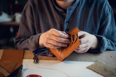 Genç bir kunduracı atölyedeki deri ayakkabılara elle dekoratif öğeler diker.