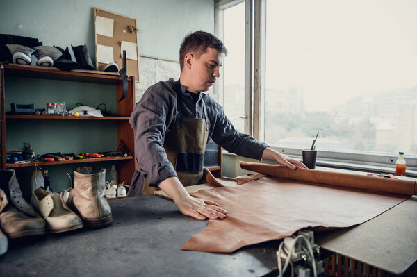 Experienced specialist in the production of footwear leather lays on a table in his workshop