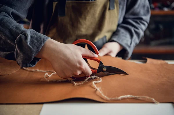 A talented young guy helps his father in the family business, cuts out blanks for shoes from leather