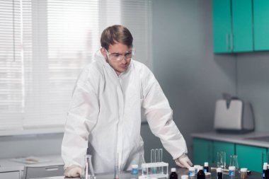 Genç düşünceli kimyager parlak bir laboratuvarda masaya yaslanıyor.