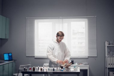 Genç bir laboratuar çalışanı öğle yemeği molası veriyor, ofisinde hamburger yiyor.