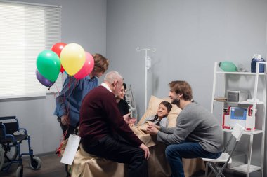 Neşeli bir aile hastane koğuşundaki küçük bir kızı ziyaret ediyor.