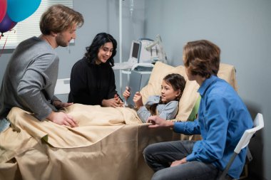 Yatağında dijital tabletle ve akrabalarıyla sağlık sorunları olan bir kız öğrenci.