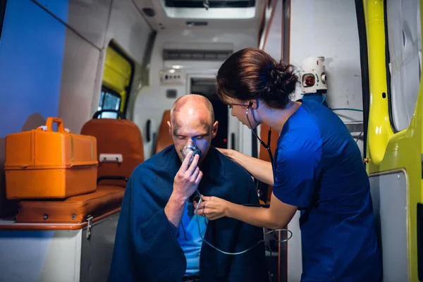 Машина скорой помощи, молодая медсестра проверяет сердцебиение раненого человека в одеяле — стоковое фото