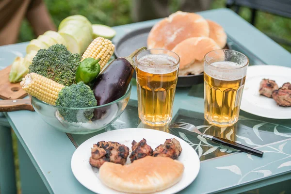 Крупный план столика для пикника в саду на двоих. Еда, мясо на гриле, овощи на гриле, пиво. — стоковое фото
