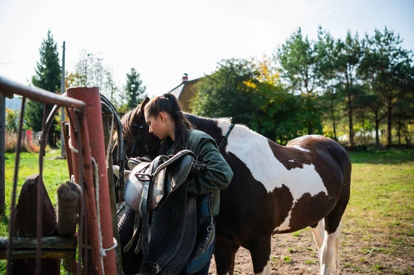 После поездки жокей снимает седло с лошади рядом с забором на ранчо. — стоковое фото
