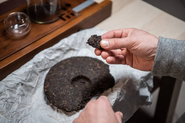 Nahaufnahme einer Männerhand und eines in eine Waschmaschine gepressten Stücks authentischen orientalischen schwarzen Tees. Auf dem Tisch für die Teezeremonie. — Stockfoto