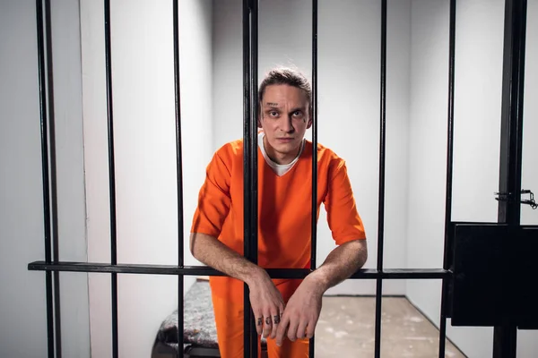 Psychological portrait of an evil and wild prisoner through the bars of a prison cell. A strong look and emotions. — Stock Photo, Image