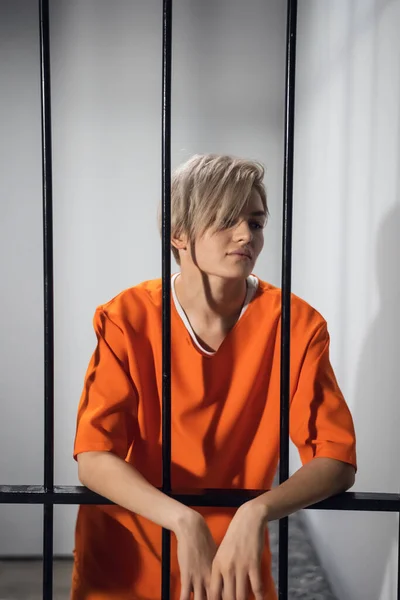 Uma rapariga bastante condenada está apoiada nas grades da cela. — Fotografia de Stock