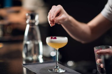 Barın üzerinde parlak sarı bir alkollü kokteyl ve gece kulübünde bir barmenin elleri olan bir bardak..