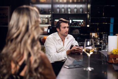 Bir adam ve bir kadın barda bir masada oturuyor, bir adamın yüzü, uzun saçlı sarışın bir kadının arkası.