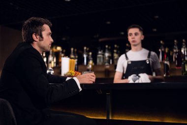 Genç bir adam barda kokteyl içer, barmenle iletişim kurar.