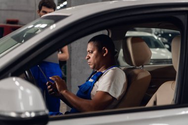 Tamirci arabada oturuyor ve tablet kullanıyor.