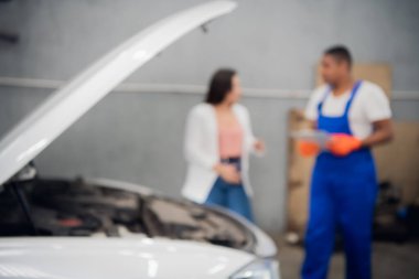 Tamircinin bulanık arkaplanı müşteriye araba tamirini sorar.