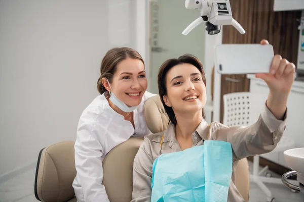 Imagen de una hermosa joven sonriente sentada en un centro de odontología médica, tomando una selfie con su teléfono inteligente — Foto de Stock