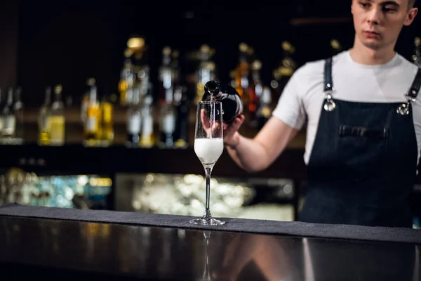 Досвідчений бармен в фартусі наповнює келих шампанського в барі — стокове фото