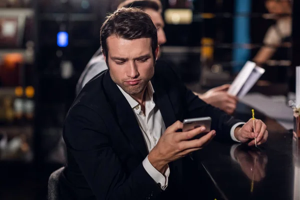 Un joven lee un mensaje en su teléfono, se sienta en un bar — Foto de Stock