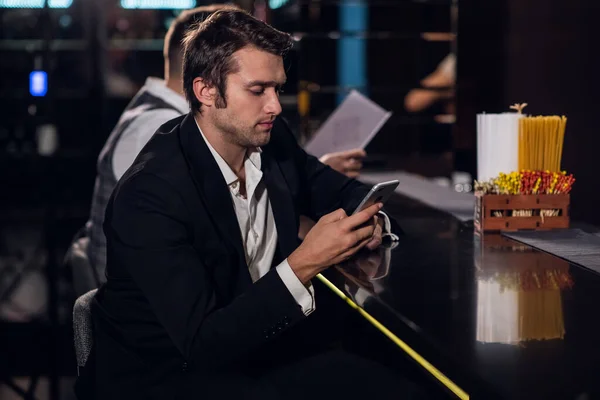 Belo jovem surfando na Internet em um smartphone atrás do bar em uma boate — Fotografia de Stock