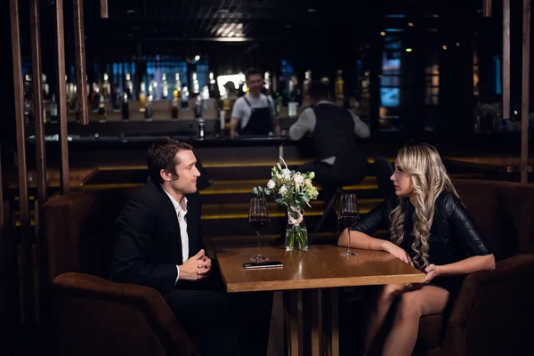 Πρώτο ραντεβού σε ένα εστιατόριο με ένα νεαρό άνδρα και μια όμορφη ξανθιά, κάθεται στο τραπέζι, πάνω στο τραπέζι ένα μπουκέτο και ένα smartphone — Φωτογραφία Αρχείου
