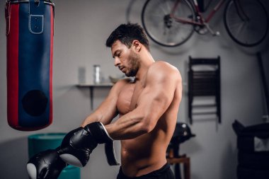 Genç bir boksör kum torbasıyla ısınmaya hazırlanıyor, eldiven takıyor..