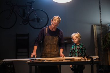 Genç bir baba ve küçük oğlu marangozların atölyesinde ağaçtan oyuncak yapıyorlar..