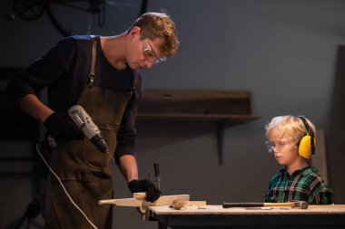 Genç bir baba ve küçük oğlu marangozların atölyesinde ağaçtan oyuncak yapıyorlar..