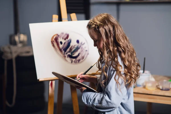 First lesson in art school, a little girl learns to draw and makes her first oil painting on canvas. — Stock Photo, Image