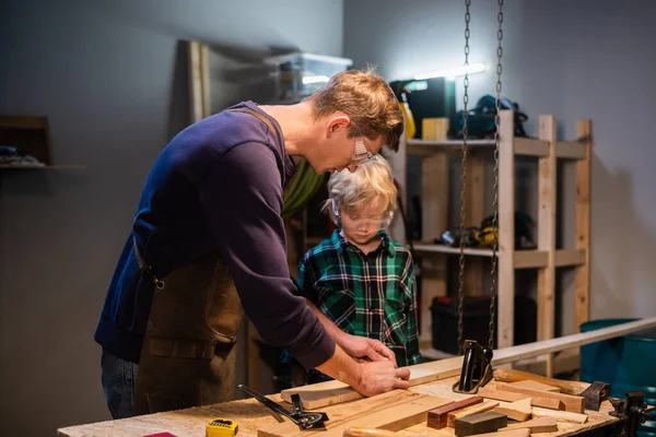 a young father teaches the basics of carpentry to his son in the garage.