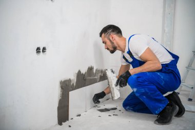 Tulumlu işçi banyo duvarına fayanslar koyuyor.