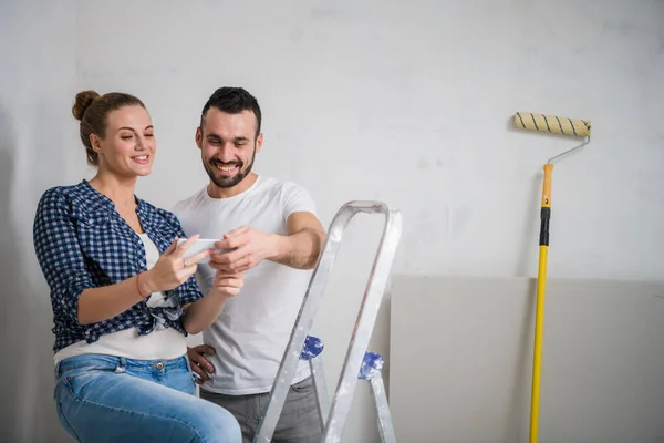 Young couple looks at photos on the phone screen. They take a break from renovation — Stock Photo, Image