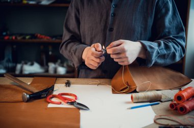 Deneyimli bir tabakçı dikişli deri bir ürün için toka diker.
