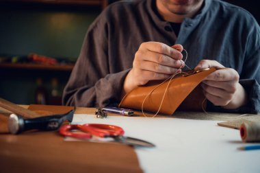 Genç bir kunduracı atölyedeki deri ayakkabılara elle dekoratif öğeler diker.
