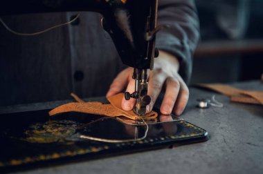Kahverengi, hakiki bir deri parçasında yüksek kaliteli bir ipliğin yakın plan fotoğrafı. Bir terzi ve dikiş makinesinin elleri