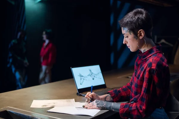 L'amministratore di un salone di tatuaggi disegna uno schizzo di un tatuaggio utilizzando un computer portatile nel laboratorio. — Foto Stock